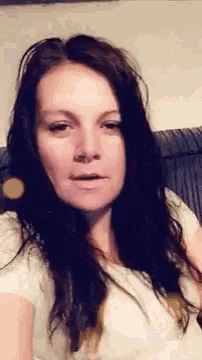 a woman with long dark hair is sitting on a couch making a funny face .