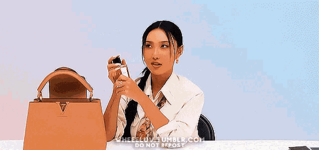 a woman is sitting at a table with a purse and holding a bottle of perfume .