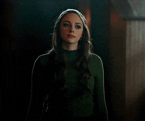a woman in a green sweater is standing in a dark room looking at the camera .