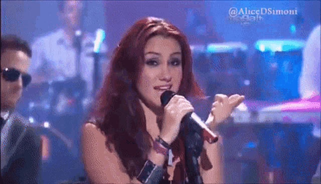 a woman with red hair is singing into a microphone with a band in the background