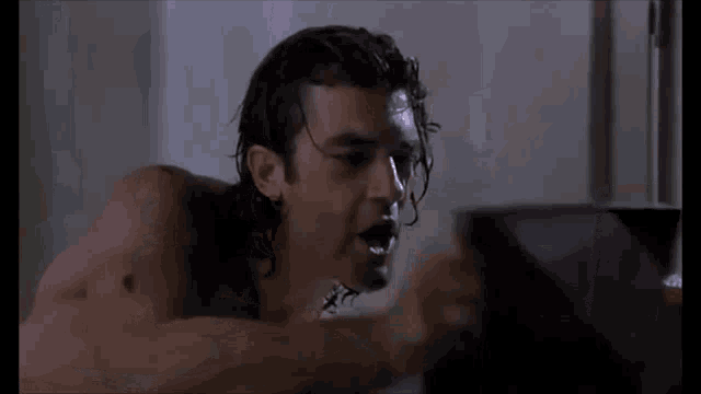 a shirtless man is laying in a bathtub and looking at a laptop .