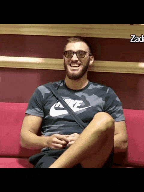 a man wearing a nike shirt sits on a couch