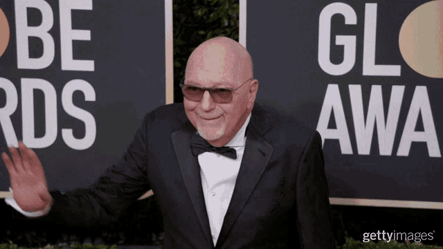 a man in a tuxedo stands in front of a sign that says be rds gl awa