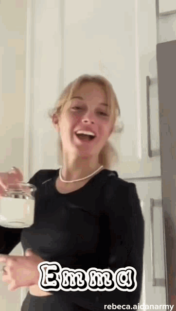 a woman in a black shirt is holding a jar of yogurt and smiling .
