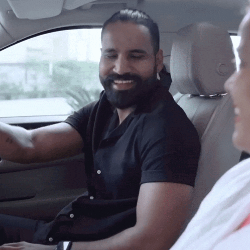 a man with a beard is driving a car and smiling