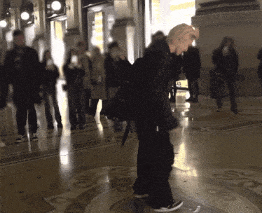 a man in a black jacket stands in front of a crowd in a hallway
