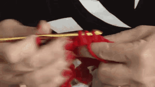 a close up of a person holding a crochet hook over a red yarn .