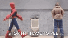 a man in a spiderman costume is walking next to a man in a urinal .