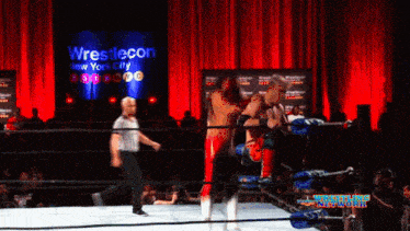 two wrestlers are in a ring with a wrestlecon sign behind them