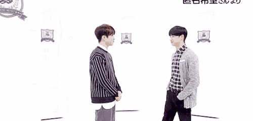 two young men are standing next to each other against a wall and one of them is hugging the other .