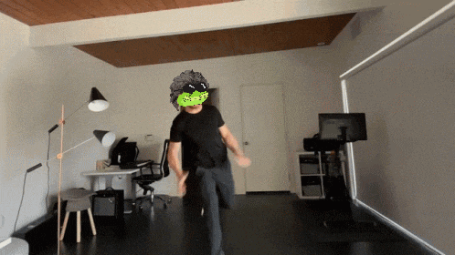 a man in a black shirt is dancing in a room with a green mask on his head