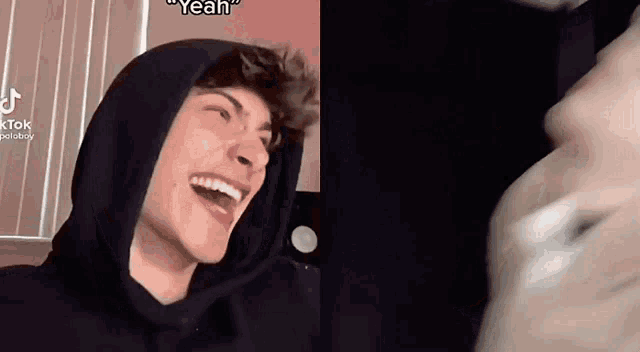 a man in a black hoodie is laughing and looking at another man 's face .