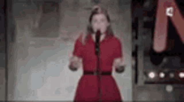 the woman is wearing a red dress and singing into a microphone .