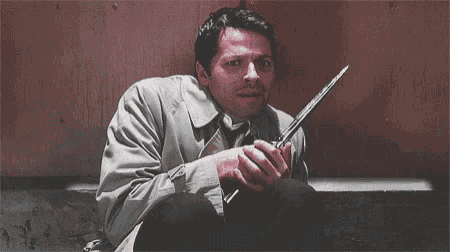 a man is holding a knife in his hand while sitting on the ground .