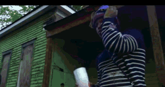 a person in a striped shirt is standing in front of a green house