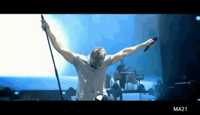 a man singing into a microphone with his arms outstretched in front of a band