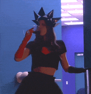 a woman wearing a black crop top and a red glove drinks from a glass