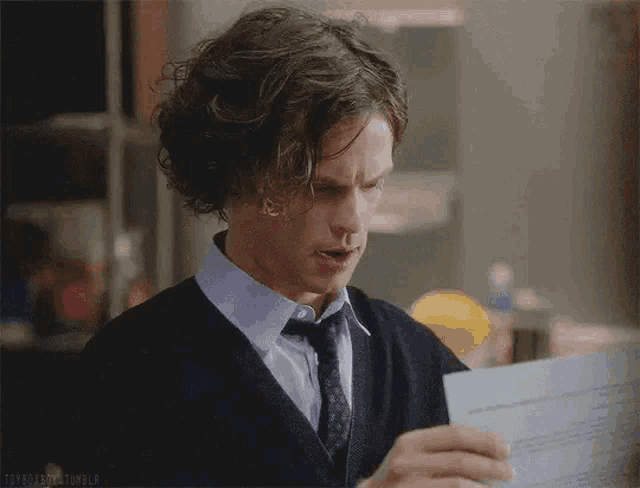a man with curly hair and a tie is looking at a laptop .