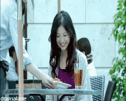 a woman sits at a table with a plate of food and a glass of tea while a man serves her food