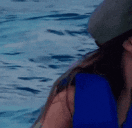 a woman wearing a blue shirt and a hat is standing in front of a body of water