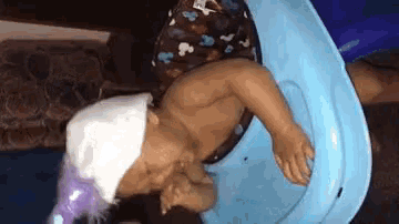 a baby wearing a white hat and a purple wig is laying on a blue toy car .