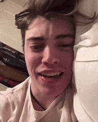 a young man is laying on a bed with his head on a pillow and his eyes closed .
