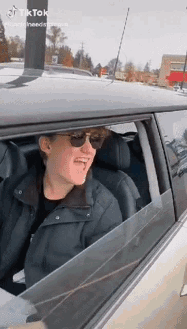 a young man wearing sunglasses is sitting in a car and making a funny face .