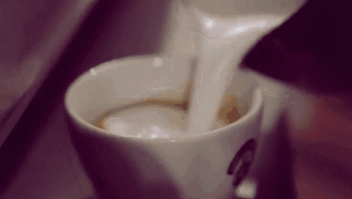 a close up of a person pouring milk into a cup of cappuccino .