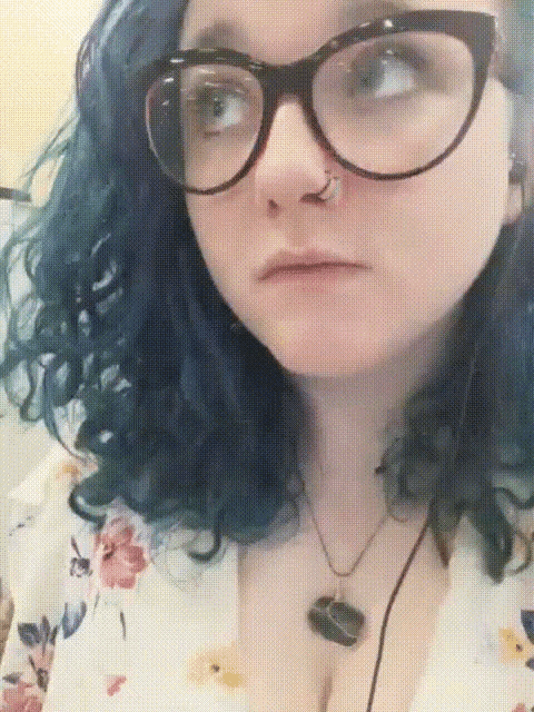 a woman with blue hair wears glasses and a necklace