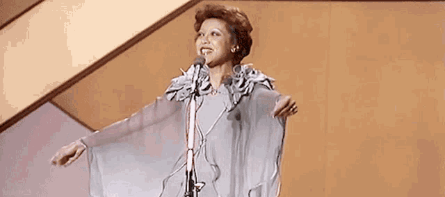 a woman is singing into a microphone with her arms outstretched