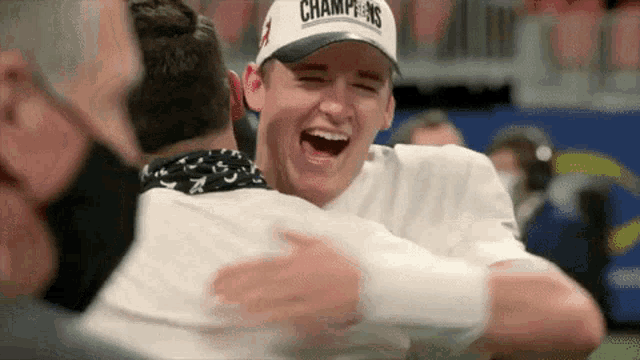 a man in a champions hat is hugging another man .