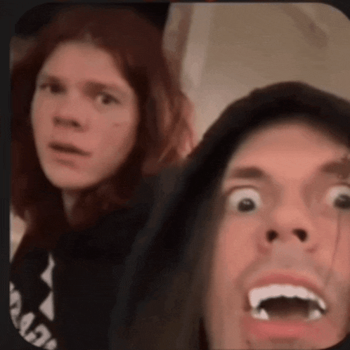 a man with long hair is making a funny face next to a woman with red hair