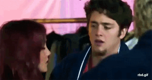 a man and a woman are kissing in a room with clothes hanging on a rack .
