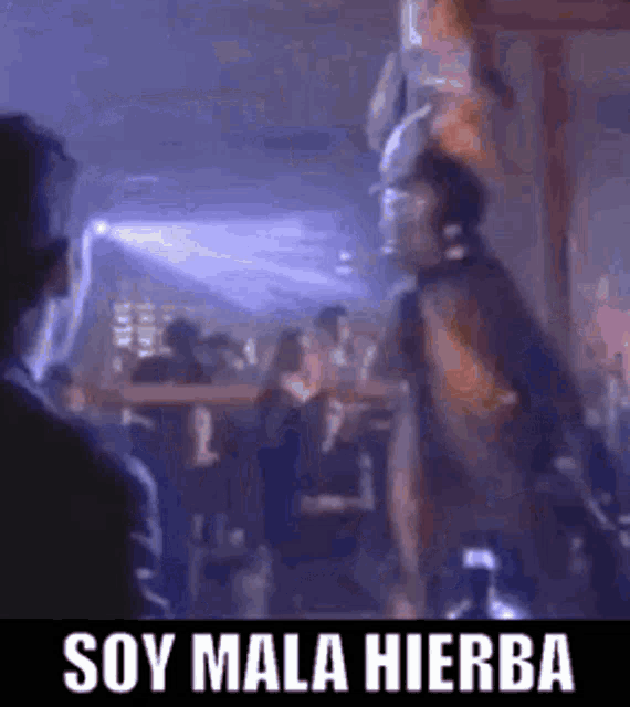 a man is dancing in a club with the words soy mala hierba on the bottom of the image .