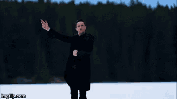 a man in a black coat is standing in a snowy field with his arms outstretched ..