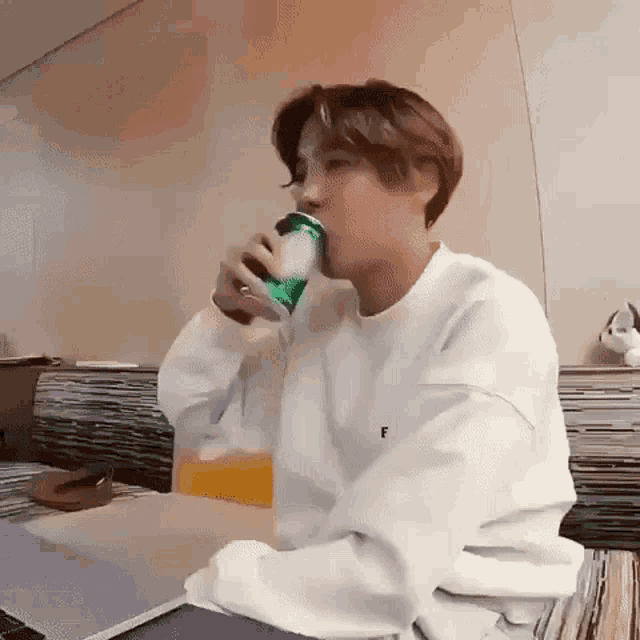 a man in a white sweatshirt is drinking a can of soda .