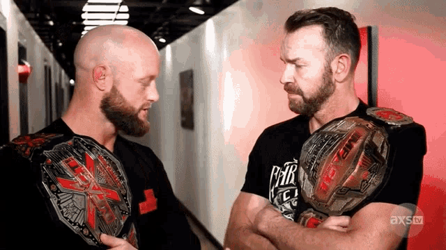 two wrestlers are standing next to each other with their arms crossed and the words axs tv on the bottom right