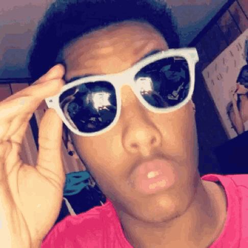 a young man wearing sunglasses and a pink shirt is making a funny face