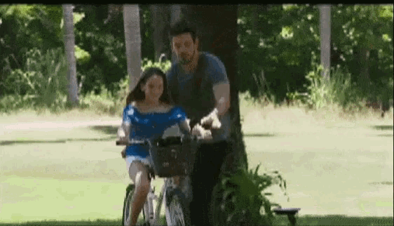 a man is pushing a little girl on a bike .
