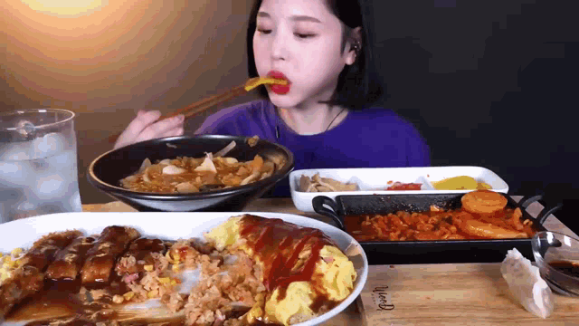 a woman is eating a bowl of food with chopsticks while sitting at a table with plates of food