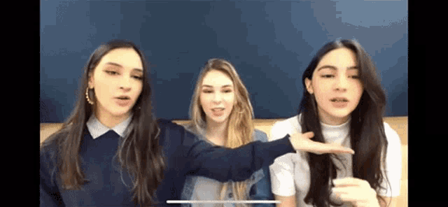 three girls are standing next to each other and one of them is pointing at the camera