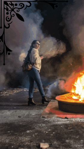 a woman standing in front of a fire with smoke coming from it