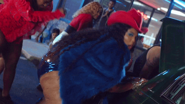 a woman wearing a red hat and a blue fur coat is standing next to a green car