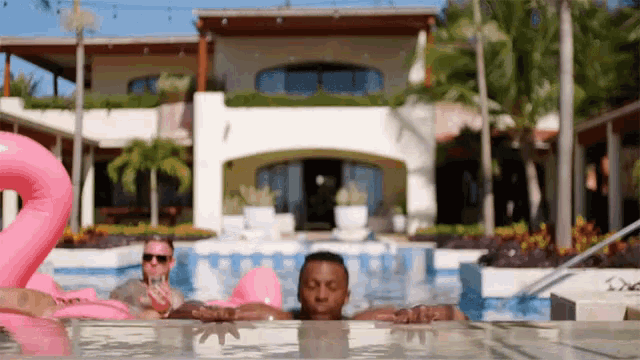 a man is laying in a pool with a pink flamingo float in the background