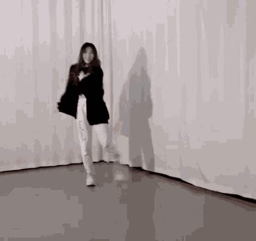 a woman in a black jacket and white pants is dancing in a dance studio .