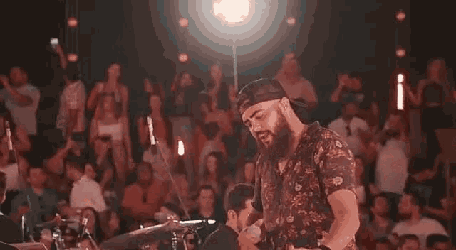a man with a beard is playing a drum set in front of a crowd of people .