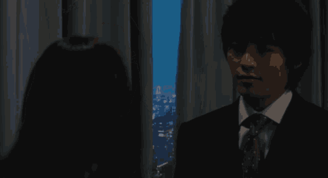 a man in a suit and tie stands next to a woman in front of a window