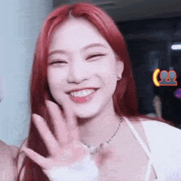 a woman with red hair is smiling and waving her hand .