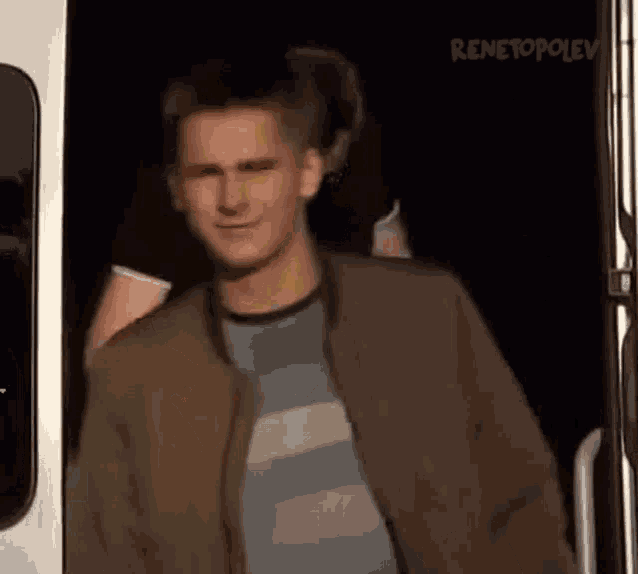 a young man in a striped shirt and jacket is walking out of a bus .