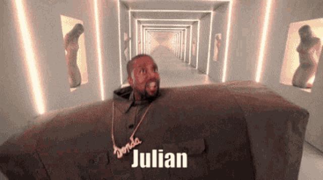 a man with a necklace that says julian is sitting in a couch .
